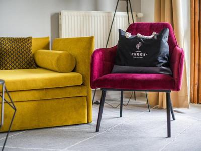 Rotes Samt-Sessel mit schwarzer Tasche neben gelbem Sofa in hellem Wohnzimmer.