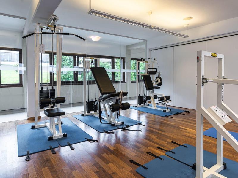 Moderner Fitnessraum mit Trainingsgeräten und Holzfußboden in einem hellen Raum.