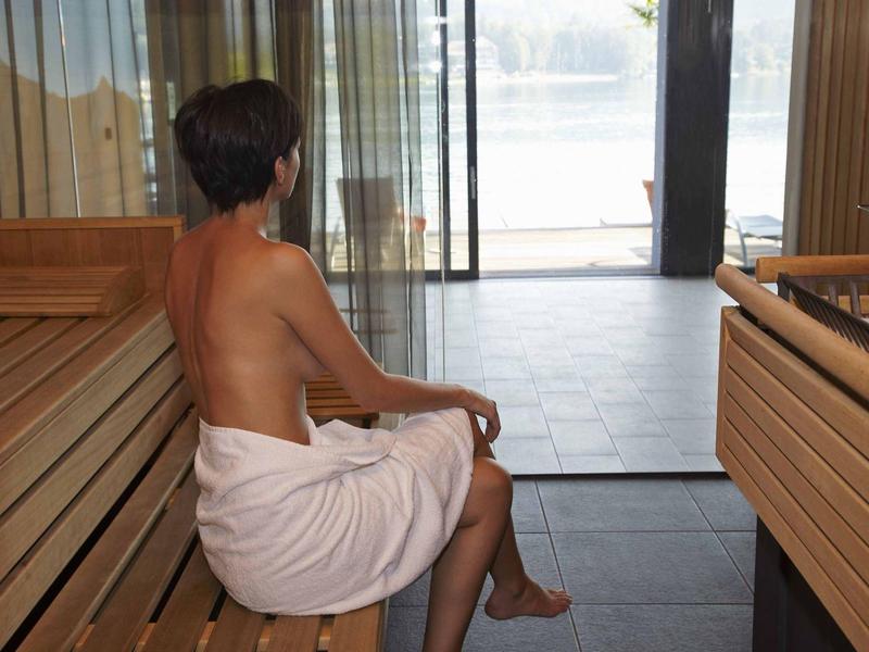 Frau mit Handtuch sitzt in einer Sauna und blickt zum Fenster mit Wasserblick.