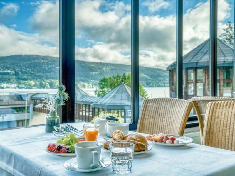 Tisch mit Frühstück vor großen Fenstern mit Blick auf Hügel und Wasser