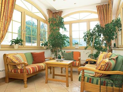 Bright living room with cushioned chairs, plants, and large windows overlooking the mountains.