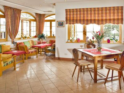 Gemütlicher Hotelraum mit Stühlen, Tischen, großen Fenstern und warmen Vorhängen.