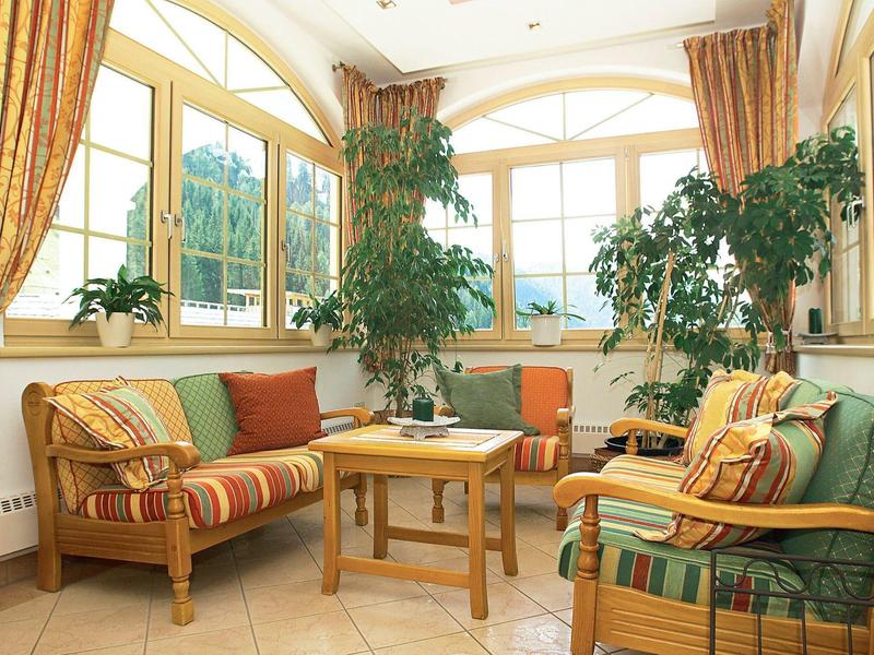 Bright living room with cushioned chairs, plants, and large windows overlooking the mountains.