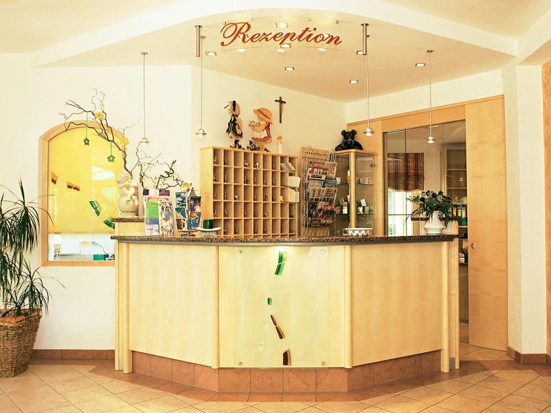 Modern hotel reception area with light wood front desk and decorative plants.