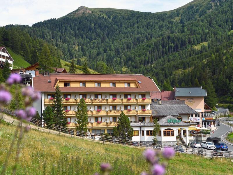 Hotel in the mountains with forested hills and meadows in the foreground