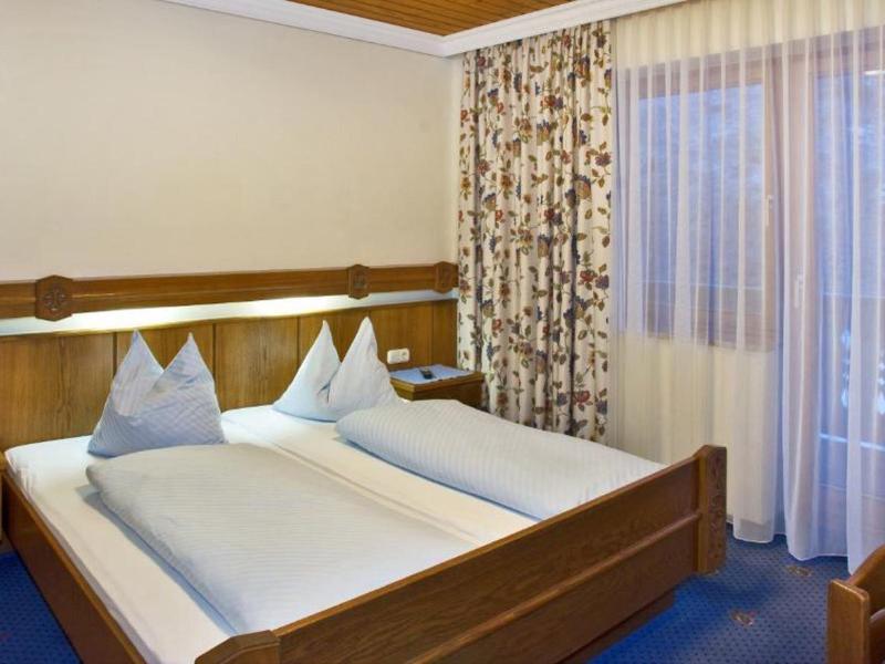 Cozy hotel room with two single beds, wooden furniture, and large windows with curtains.