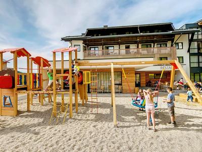 Speelplaats met klimrek, schommel en kinderen voor een meerlaagse hotelgebouw op een zonnige dag