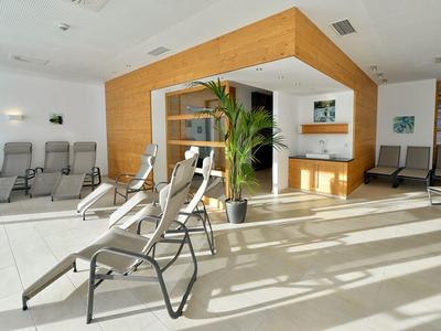 Lichte ontspanningsruimte met ligstoelen, planten en houten wandpanelen in de wellnessruimte.