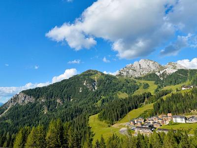 Paisaje montañoso con bosque verde, cielo azul y pequeño asentamiento de casas de vacaciones.