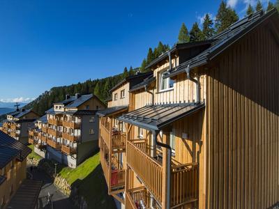 Holzchalets mit Balkonen in bergiger Umgebung bei klarem Himmel.
