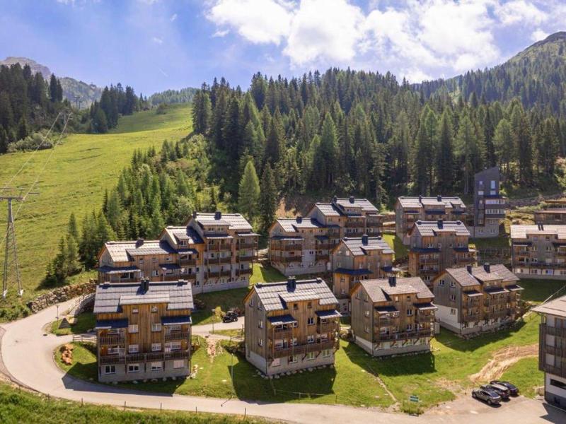 Bergdorp met chalets in groene vallei en beboste heuvels onder een blauwe lucht.