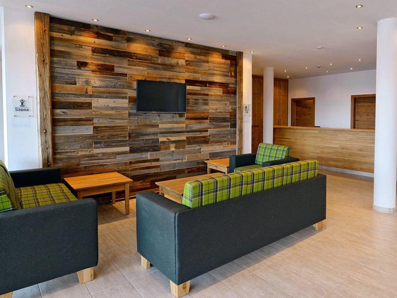 Moderne hotel lounge met houten wandbekleding, tv en gestoffeerde sofa's in gedempte kleuren.
