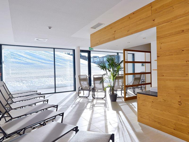 Lichte ontspanningsruimte met ligstoelen en panoramische ramen met uitzicht op bergen.