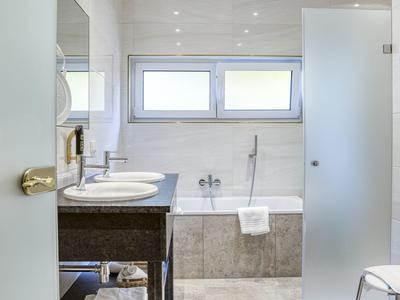 Modernes Badezimmer mit Badewanne, zwei Waschbecken und frostsicherer Glastür.