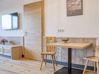 Heller Hotelraum mit Holzfußboden, kleinem Tisch, zwei Stühlen und wandmontiertem Fernseher.