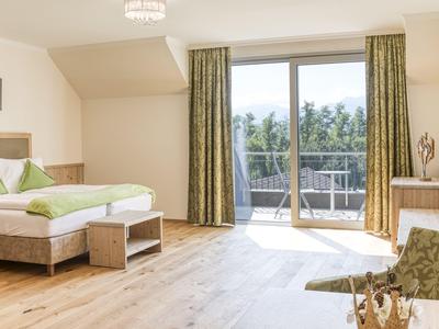 Helles Hotelzimmer mit Holzboden, Doppelbett und Balkon mit Blick auf grüne Landschaft.