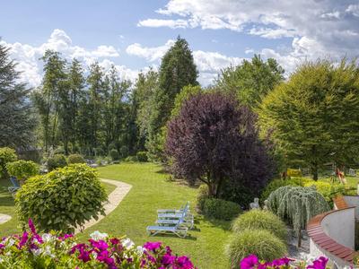 Ein gepflegter Garten mit bunten Blumen, Bänken und einem Weg bei sonnigem Wetter.