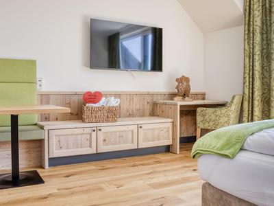 Gemütliches Hotelzimmer mit hellem Holzboden, grünem Vorhang und moderner Einrichtung.