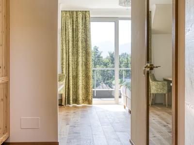 Heller Hotelkorridor mit Holzboden, offener Tür und Blick auf einen Balkon mit grüner Landschaft.