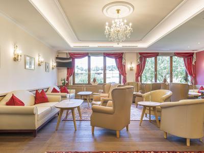 Helle Hotellounge mit bequemen Sesseln, Sofas und großen Fenstern mit rotem Vorhang.