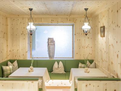 Gemütlicher Hotel-Aufenthaltsraum mit Holzverkleidung, grünen Sitzbänken und weißen Tischtüchern.