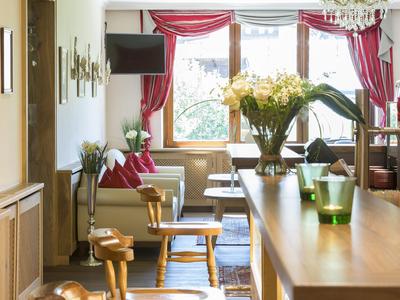 Heller Hotel-Loungebereich mit Holzmöbeln, Blumen und großen Fenstern mit roten Vorhängen.