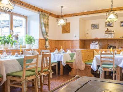 Helles Restaurant mit Holzmöbeln, weißen Tischdecken und großen Fenstern mit Pflanzen.