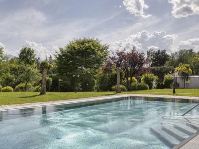 Klare blaue Pool mit Stufen und grünen Bäumen im Hintergrund unter bewölktem Himmel.
