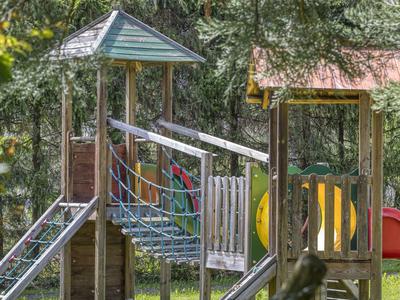 Holzspielplatz mit Rutschen und Kletterelementen in einem schattigen Gartenbereich.