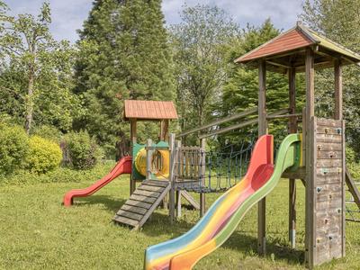 Bunter Kinderspielplatz mit Rutschen und Klettergeräten in einem grünen Park bei sonnigem Wetter.