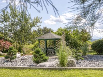 Grüner Garten mit einer kleinen, hölzernen, sechseckigen Laube und gepflegtem Kiesbett.