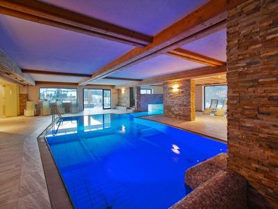 Indoor pool in a modern wellness area with stone walls and large windows.