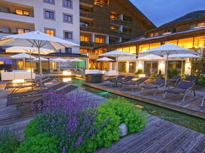 Hotel terrace with loungers, umbrellas, and lit windows at dusk.
