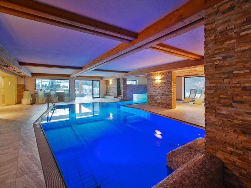 Indoor pool in a modern wellness area with stone walls and large windows.