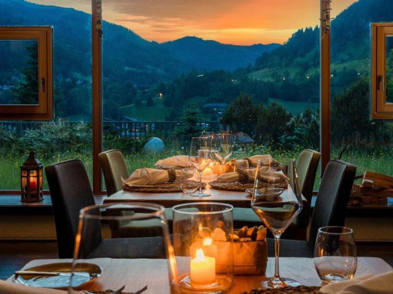 Elegant set table by panoramic windows overlooking green valley at sunset.