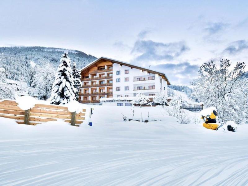 A hotel surrounded by snow-covered trees and mountains under a cloudy sky.