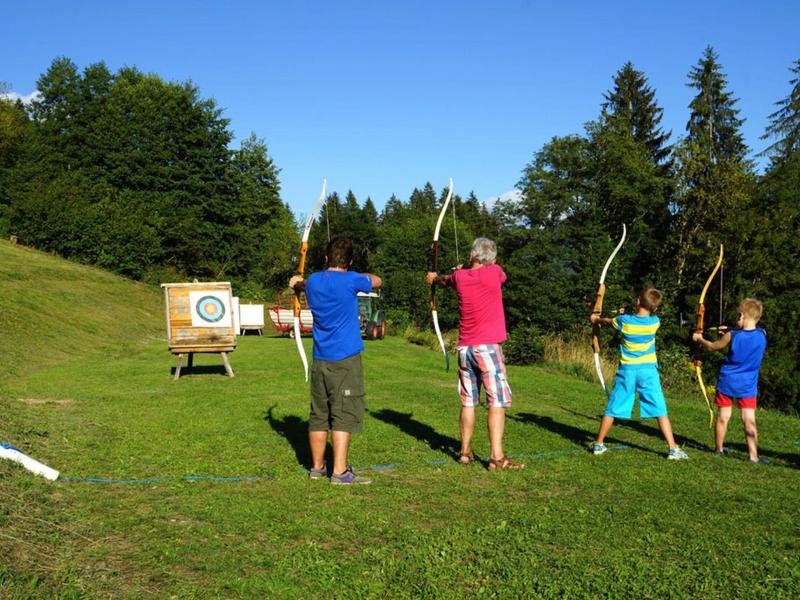 Quattro persone praticano il tiro con l'arco su un campo verde sotto un cielo limpido.