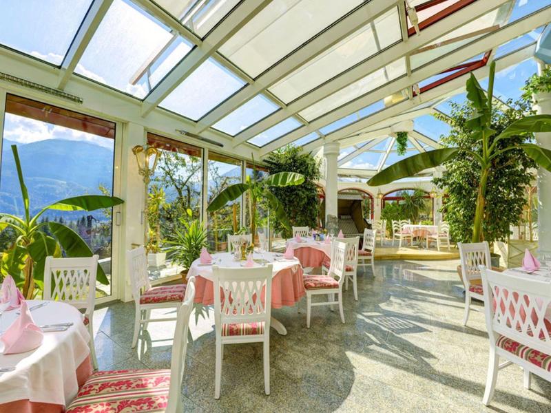 Ampia terrazza luminosa con mobili bianchi, piante e vista sulle montagne in una giornata di sole.