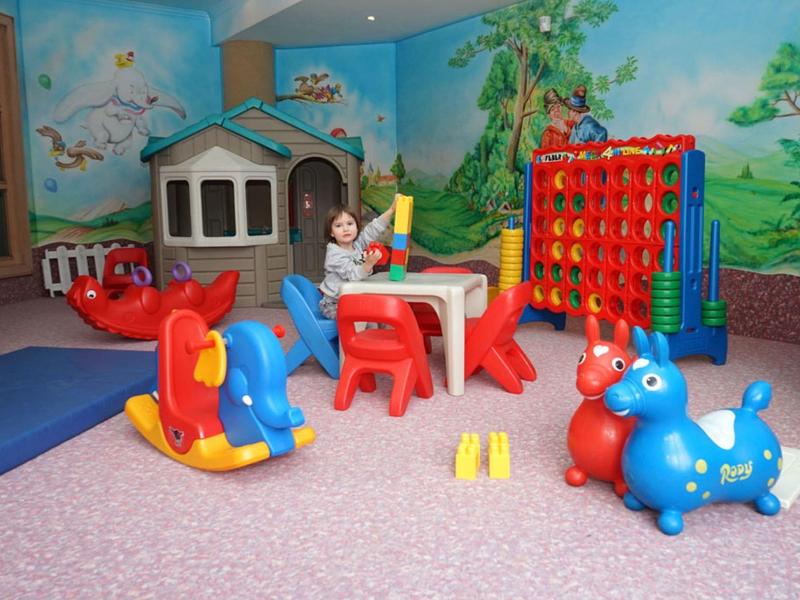 Colorata stanza giochi per bambini con casetta, tavoli, sedie e vari giocattoli.