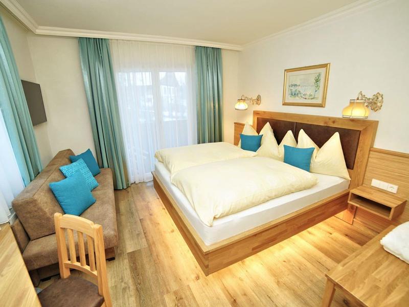 Camera d'albergo accogliente con letto matrimoniale, divano, scrivania e grande finestra con tende.