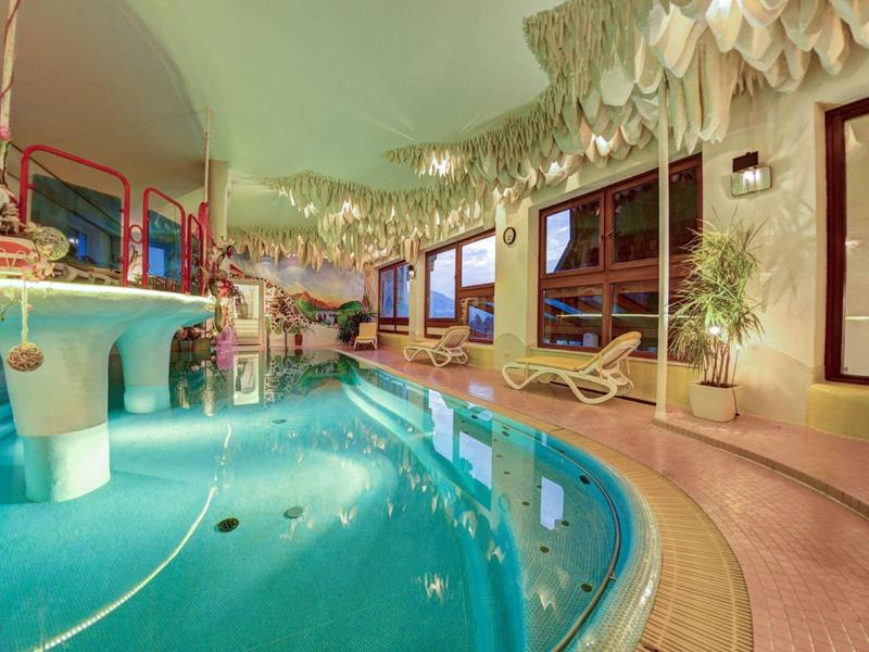 Piscina interna con sdraio, piante e soffitto decorativo in un hotel