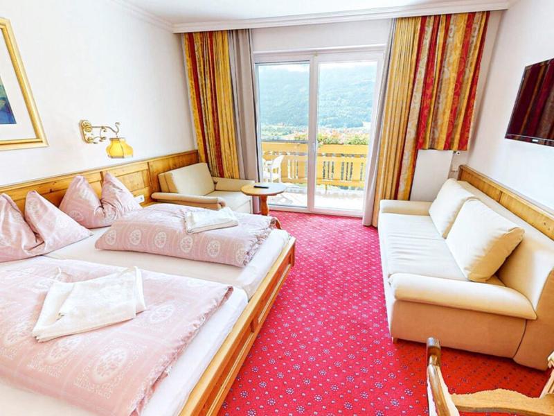 Camera d'hotel luminosa con letto matrimoniale, divano, balcone e finestra panoramica.