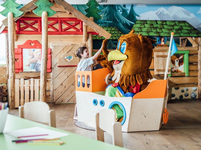 Aire de jeux intérieure avec un enfant en costume d'ours sur un véhicule jouet coloré.