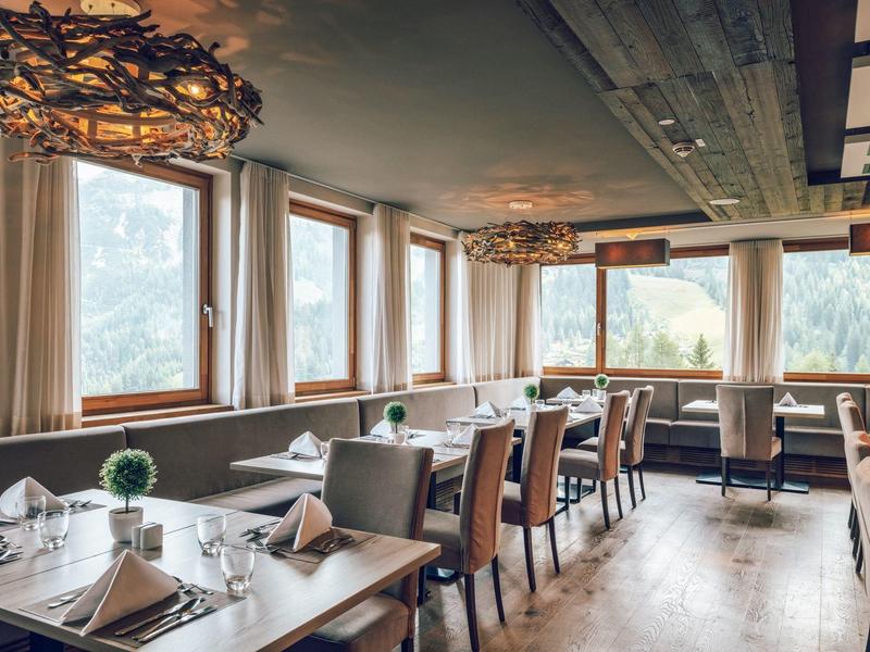 Intérieur de restaurant confortable avec tables en bois et grandes fenêtres donnant sur des arbres.