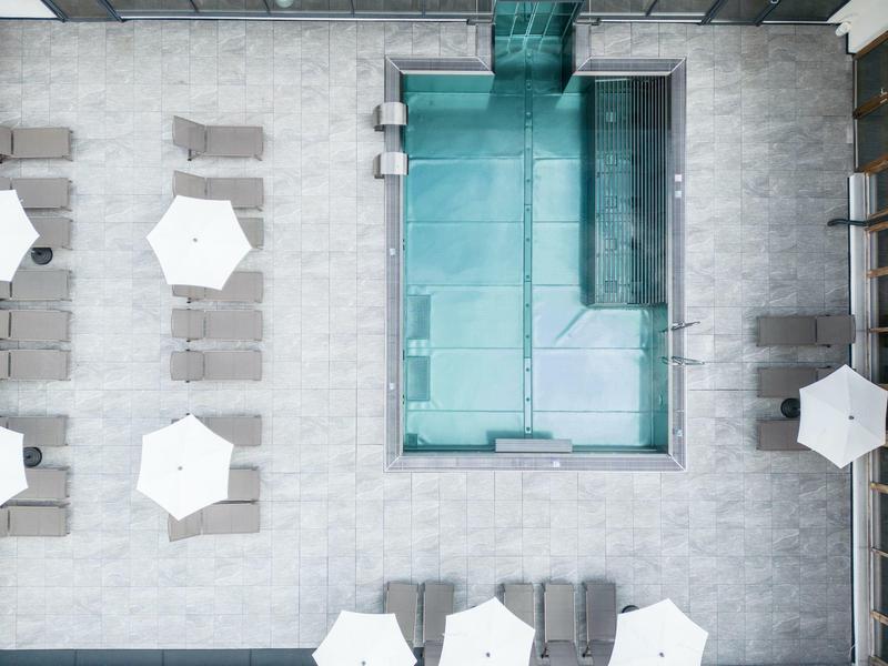 Vue de dessus d'une piscine élégante avec chaises longues et parasols sur une terrasse carrelée.