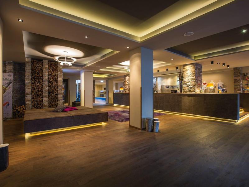 Hall d'hôtel moderne avec sol en bois, coin salon confortable et comptoir d'accueil éclairé.