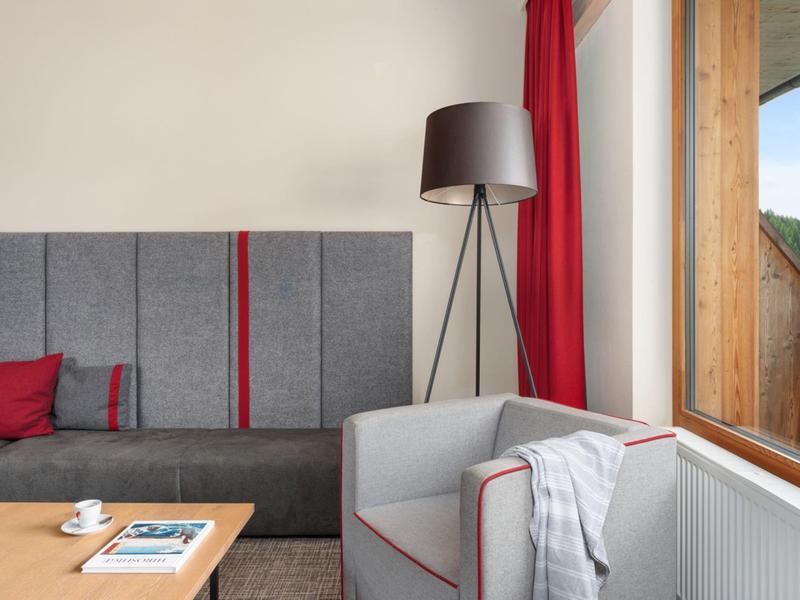 Coin de chambre d'hôtel confortable avec canapé gris, fauteuil, lampadaire, table en bois et grande fenêtre.