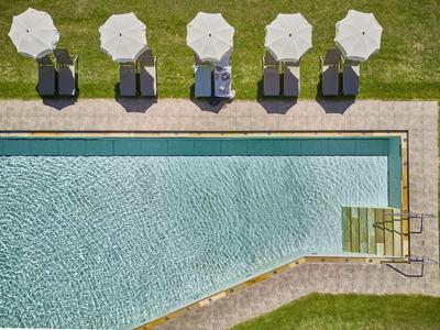 Vista aerea di una piscina limpida con sdraio e ombrelloni sull'erba.