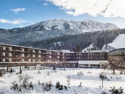 Hotelgebäude vor schneebedeckten Bergen unter blauem Himmel mit Wolken.