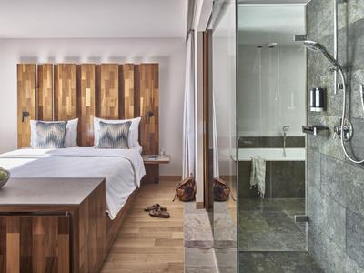 Modernes Hotelzimmer mit Doppelbett und Glas-Duschwand neben Holzmöbeln.